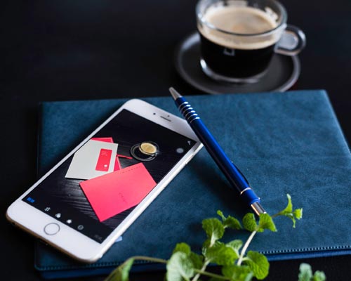 cell-phone and pen on a blue microfiber cloth with a coffee in front